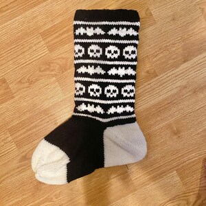 May include: Black and white knitted sock with a skull and bat pattern.