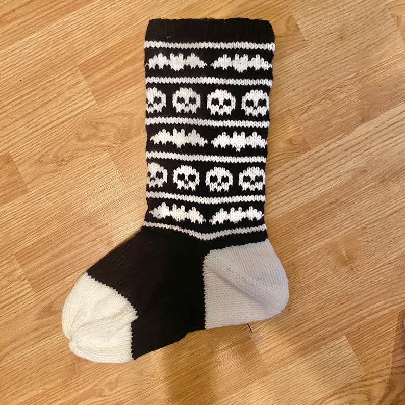 May include: Black and white knitted sock with a skull and bat pattern.