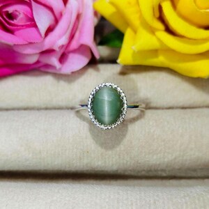 Op de afbeelding: Een zilveren ring met een groene ovale edelsteen gezet in een decoratieve zilveren zetting. De ring wordt getoond op een witte achtergrond.