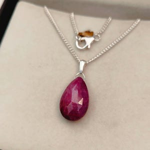 Könnte beinhalten: Eine silberne Kettenkette mit einem tropfenförmigen Anhänger mit einem facettierten Rubin-Edelstein.