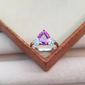 May include: A silver ring with a pear-shaped amethyst gemstone surrounded by smaller pink and white gemstones.