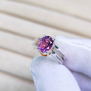 May include: A silver ring with a purple oval gemstone set in a prong setting. The ring has a triple band design.