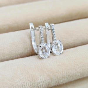 May include: A pair of silver hoop earrings with a clear oval-shaped gemstone and a row of small clear stones on the hoop.