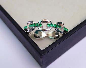Könnte beinhalten: Ein silberner Ring mit einem Kettenglied-Design. Der Ring ist mit kleinen grünen Edelsteinen besetzt.