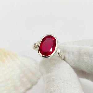 Könnte beinhalten: Ein silberner Ring mit einem großen ovalen Rubin-Edelstein. Der Ring hat ein schlichtes Design mit einer glatten Band.