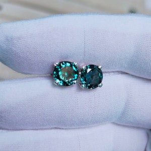 May include: A pair of silver stud earrings with round, teal-coloured gemstones.