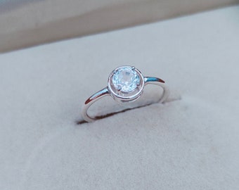May include: A silver ring with a clear round gemstone set in a bezel setting.