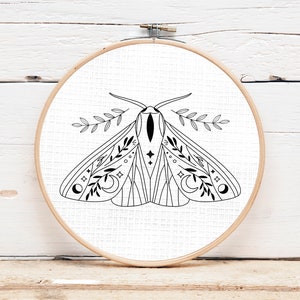 May include: Black and white line art illustration of a moth with floral and celestial details, framed in a wooden embroidery hoop.