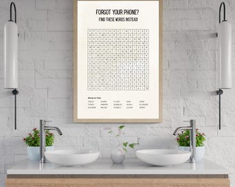 Könnte beinhalten: Ein gerahmtes Wortsuchrätsel mit dem Text "FORGOT YOUR PHONE? FIND THESE WORDS INSTEAD!" wird über einem Badezimmerwaschbecken angezeigt. Das Rätsel enthält Wörter wie TOILET, SHOWER und FLUSH. Der Rahmen hat eine hellbraune Farbe.