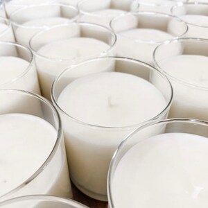 May include: A close-up view of multiple clear glass candle jars filled with white wax. The candles are arranged in a grid pattern, creating a visually appealing and symmetrical display.