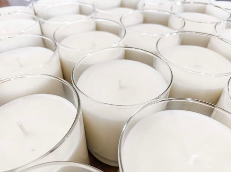 May include: A close-up view of multiple clear glass candle jars filled with white wax. The candles are arranged in a grid pattern, creating a visually appealing and symmetrical display.