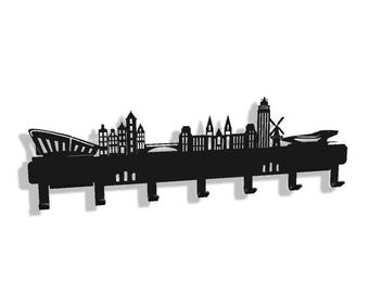May include: Black metal wall-mounted coat rack featuring a stylized cityscape silhouette. The design includes iconic buildings, a bridge, and a windmill, with multiple hooks for hanging items. The rack is approximately 30 inches wide.