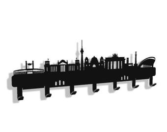 May include: Black metal key holder shaped like the Berlin skyline. The holder has six hooks for hanging keys.