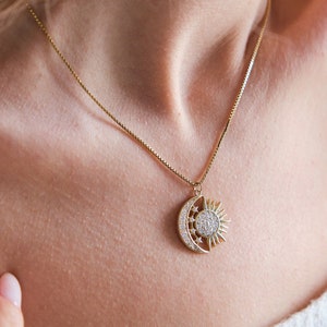 May include: A gold necklace with a crescent moon and sun pendant adorned with sparkling clear stones.