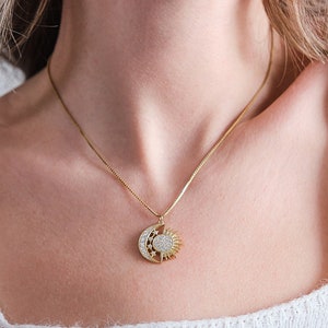 May include: A gold necklace with a sun and moon pendant featuring a clear crystal design.