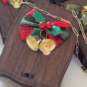 May include: A wooden box with a red and green plaid bow and two gold bells. The box has a chain attached to it.