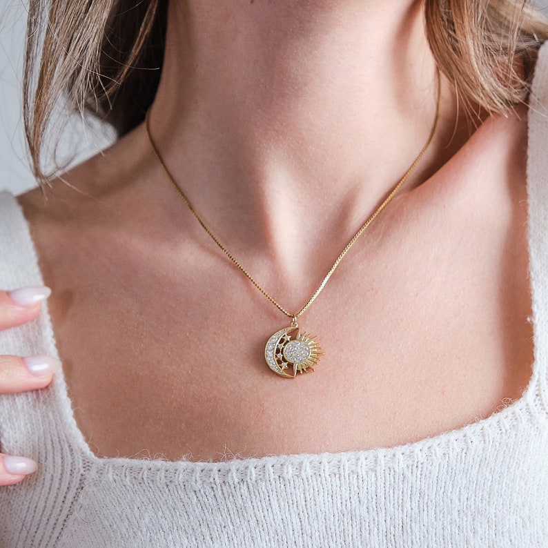 May include: A gold necklace with a sun and moon pendant featuring a clear crystal design.