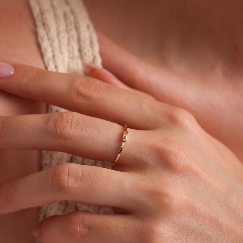 May include: A delicate gold ring with a single, small, rectangular, light pink gemstone.