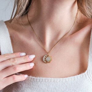 May include: A gold necklace with a sun and moon pendant featuring a sparkling crystal design.