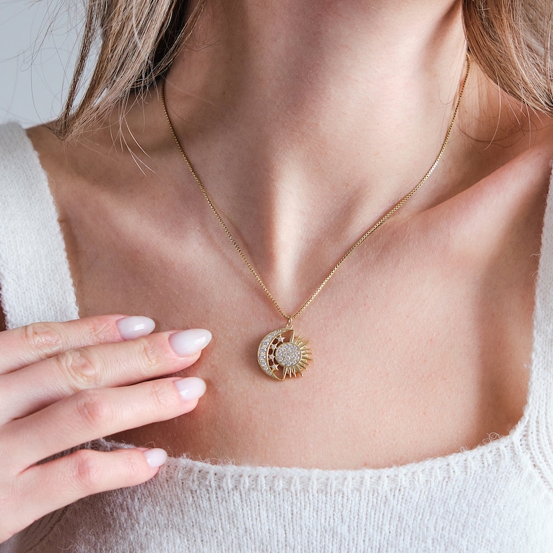 May include: A gold necklace with a sun and moon pendant featuring a sparkling crystal design.