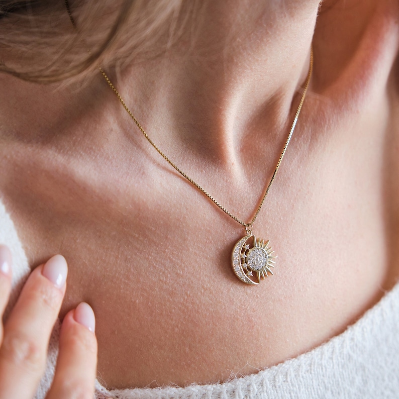 May include: A gold necklace with a crescent moon and sun pendant adorned with sparkling clear stones.