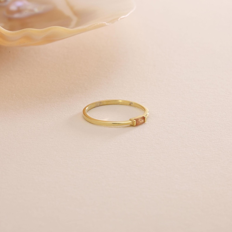 May include: A gold ring with a small, rectangular, light brown gemstone set in the band.