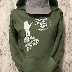 Pode incluir: Uma camisola de capuz verde com um gr&aacute;fico branco de uma pessoa a pescar em cima de um baixo. O gr&aacute;fico tamb&eacute;m inclui o texto "Bendin Tips & Rippin Lips".