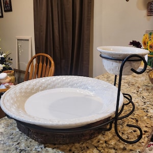 May include: A white ceramic serving dish with a woven pattern sits on a wooden base with a black metal stand. A smaller white ceramic bowl with a woven pattern sits on the stand.