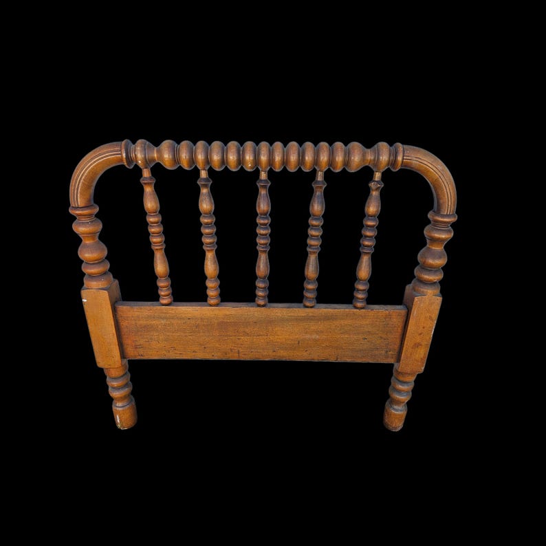May include: Wooden headboard with a warm brown finish. The headboard features a curved top with a series of small, rounded beads. Vertical spindles and turned posts add to the vintage aesthetic. The headboard is designed for a bed frame.