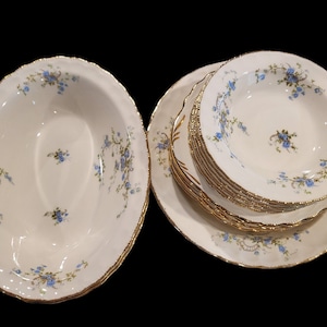 May include: A set of white porcelain bowls with a delicate blue floral pattern and gold trim. The bowls are stacked and ready to serve.