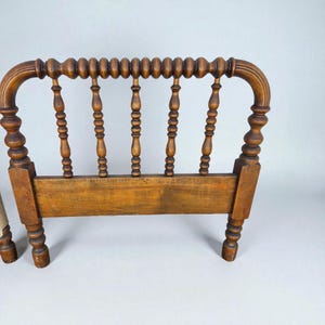 May include: A vintage wooden headboard with a warm, medium-brown finish. The headboard features a series of vertical spindles and a curved top rail with a beaded design. The legs are intricately carved, showcasing a classic, antique aesthetic.