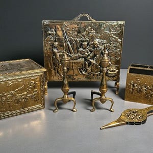 May include: A collection of antique brass fireplace accessories. Includes a rectangular screen, a box, a magazine holder, a pair of andirons, and a bellows. Each piece features detailed relief carvings and a warm, golden hue.