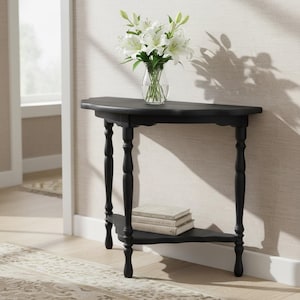 May include: A black semi-circular console table with four slender, turned legs and a lower shelf. Two stacked books rest on the shelf, and a clear glass vase filled with white lily flowers sits on the flat top surface of the table.