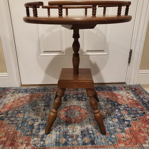 May include: A round wooden side table with a raised, decorative railing around the top. The table has a single pedestal base with a turned spindle and four turned legs.