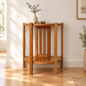 May include: A semi-circular wooden console table with a warm oak finish, featuring four vertical legs and a lower shelf. The back panel has three vertical slats. A small white vase with green foliage and a gold bowl sit on the top surface.