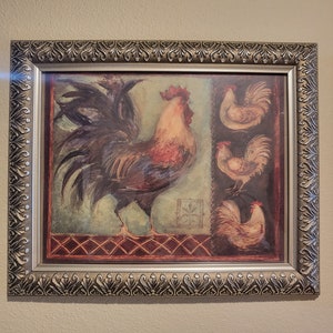 May include: A framed wall art piece featuring a large rooster on the left and three smaller roosters stacked vertically on the right. The artwork uses a palette of brown, tan, and muted green tones, enclosed in a decorative metallic silver frame.