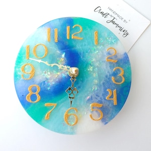 May include: A blue and green resin clock with gold numbers and hands. The clock is handmade by Craft Jamming.