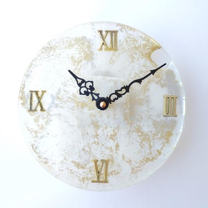 May include: White resin clock face with gold flecks and black Roman numeral hour markers. The clock hands are black.