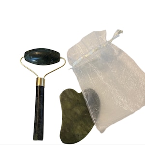 May include: A jade facial roller, a gua sha tool, and a small white drawstring bag are displayed against a white background. The roller has a dark green stone and gold-colored metal accents. The gua sha is a similar green color.