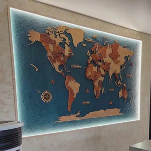 Peut inclure: Une grande carte du monde en bois, montée sur un mur, avec des continents en différentes nuances de marron et un fond bleu océan. La carte comprend de petites découpes en bois d'avions, de boussoles et de bateaux. La carte est encadrée d'une bordure blanche et éclairée d'une lumière douce.