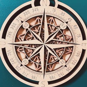 May include: A wooden compass with a brown and black color scheme. The compass has a circular shape with a black outer ring and a brown inner ring. The compass face has a detailed design with a starburst pattern and a compass rose with the directions N, S, E, W, NE, NW, SE, and SW. The compass face also has numbers from 0 to 360 degrees.