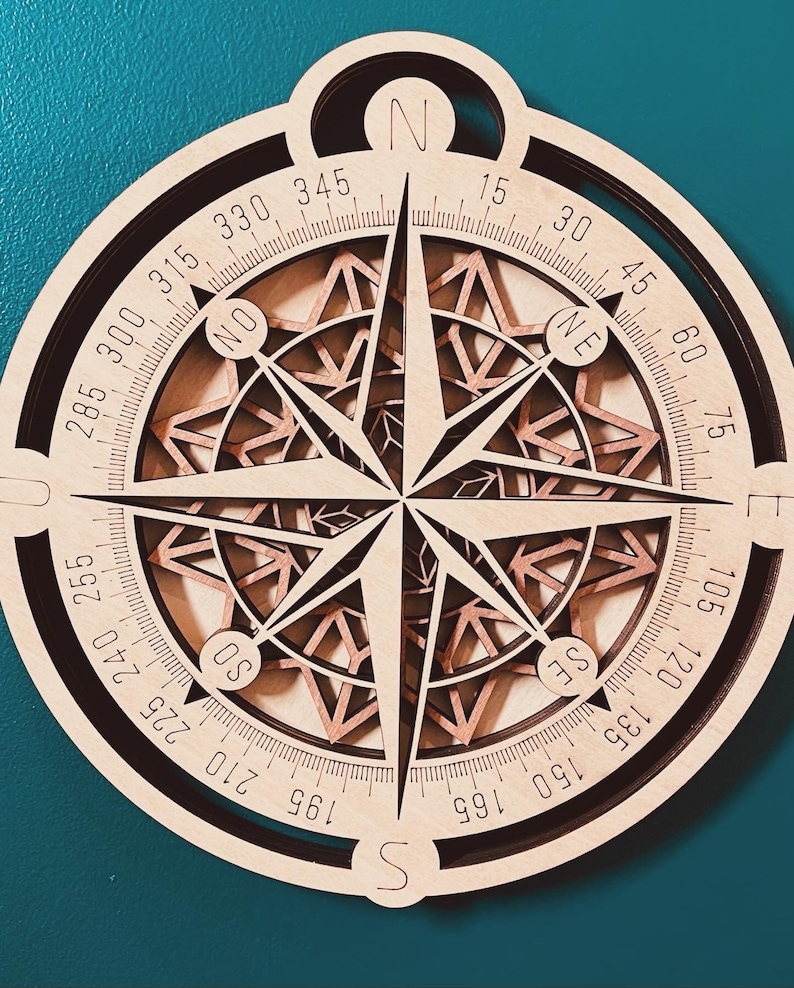 May include: A wooden compass with a brown and black color scheme. The compass has a circular shape with a black outer ring and a brown inner ring. The compass face has a detailed design with a starburst pattern and a compass rose with the directions N, S, E, W, NE, NW, SE, and SW. The compass face also has numbers from 0 to 360 degrees.