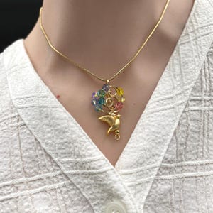 May include: A gold-toned snake chain necklace featuring a pendant with a small gold-toned bird figure suspended below a cluster of multicolored, translucent, faceted beads arranged in a circular wire frame design.