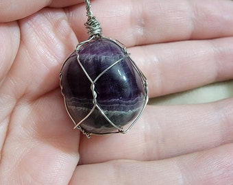 Puede incluir: Un colgante de piedra preciosa púrpura y gris envuelto en alambre de plata.