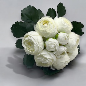 May include: A bouquet of white ranunculus flowers with green leaves.