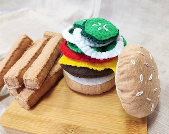 May include: A felt toy hamburger with lettuce, tomato, cheese, and pickle, along with a side of felt french fries on a wooden cutting board.