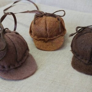 Pode incluir: Tr&ecirc;s chap&eacute;us de feltro em cores castanho e bege. Cada chap&eacute;u tem uma aba e um la&ccedil;o no topo. Os chap&eacute;us est&atilde;o pendurados numa corda.