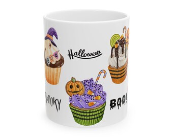 May include: White ceramic mug featuring Halloween-themed cupcake illustrations. The cupcakes have various designs, including a witch hat, a pumpkin, and candy. The mug also has the words "Halloween", "Spooky", and "Boo!"