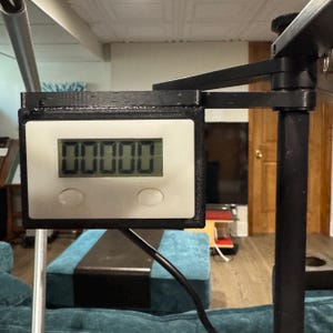 May include: A black and white digital counter with a black plastic frame and two buttons. The counter is mounted on a black metal arm.