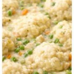 May include: A close-up shot of chicken and dumplings in a white pot. The dish includes fluffy, golden dumplings, chicken pieces, green peas, and orange carrots in a creamy sauce. The pot is white with a dark blue rim.